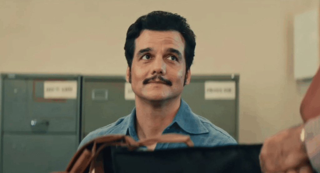 Wagner Moura sentado em uma sala, olhando para alguém de baixo para cima.